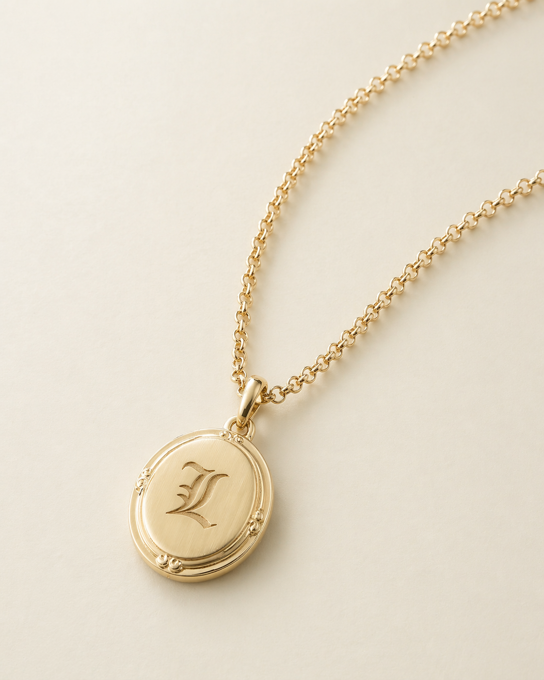 Gold necklace with a round pendant featuring the letter 'L' on a light beige background

